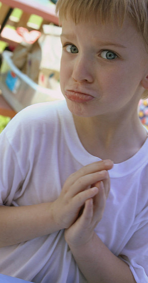A child begs with hands pleading and lower-lip poked in a pouting expression.